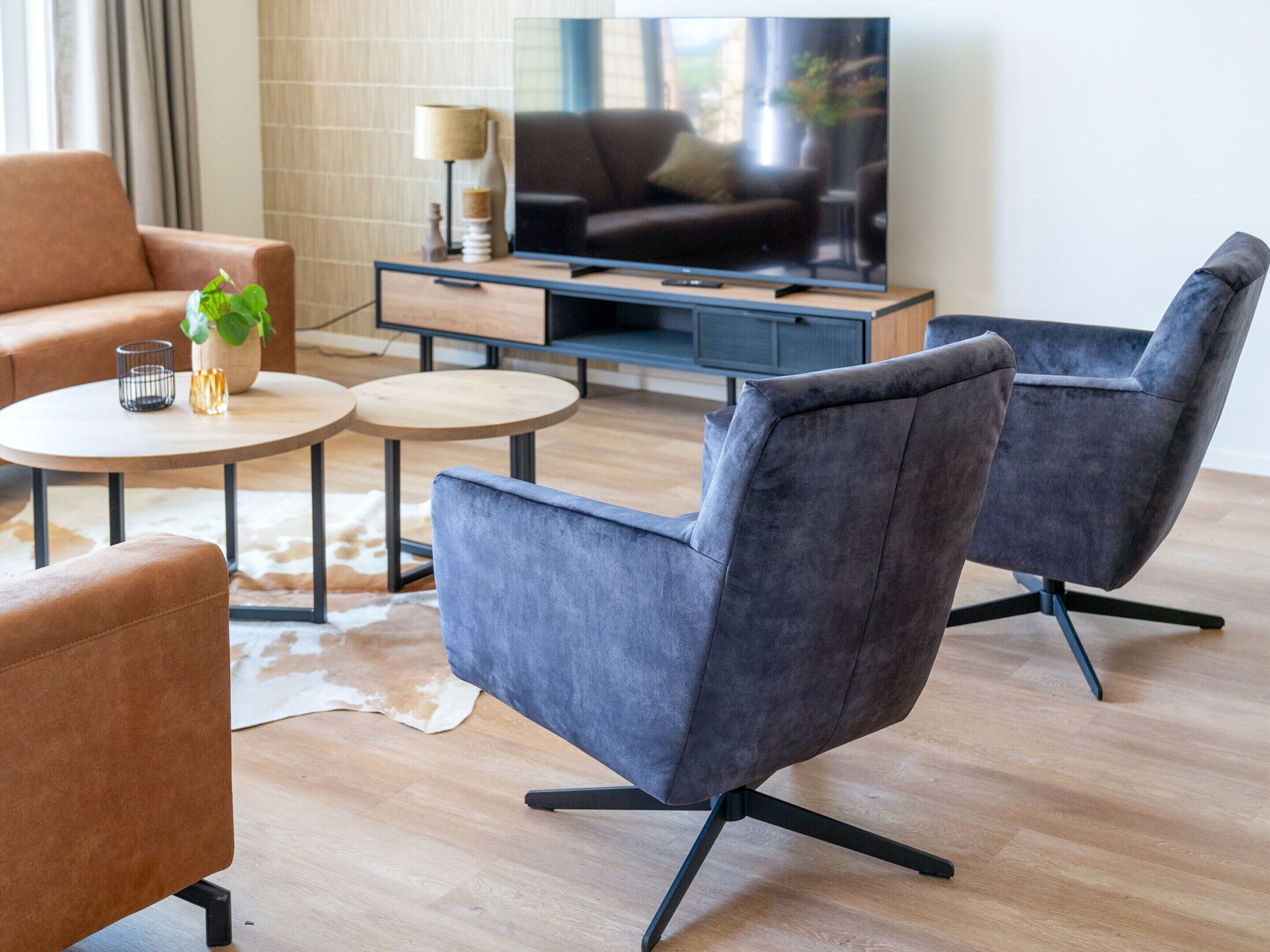 A modern living room with a sofa, two armchairs, a coffee table, and a TV.