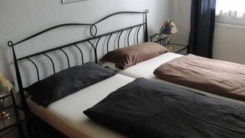 A double bed with a metal frame, two pillows, a bedside table with a lamp, and a window with curtains.