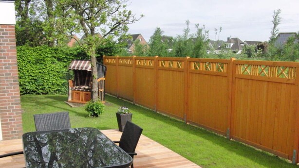 A patio with a glass-top table and chairs, surrounded by a wooden fence and a well-maintained lawn. - Karlo 4 Modern Retreat (Büsum)