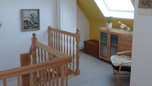 Une pièce avec un escalier en bois, une lucarne, un meuble avec des portes en verre, un panier en osier et une chaise.