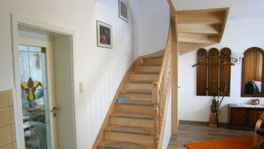 Un escalier avec des marches en bois et une rampe, menant à un palier où se trouvent un miroir et une petite table sur laquelle est posé un vase.