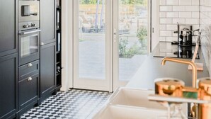 A modern kitchen with dark cabinets, a black and white checkered floor, a large window with a view of a canal, and a coffee machine. - Oceanhouse Comfortable Holiday Residence (Wieringerwerf)