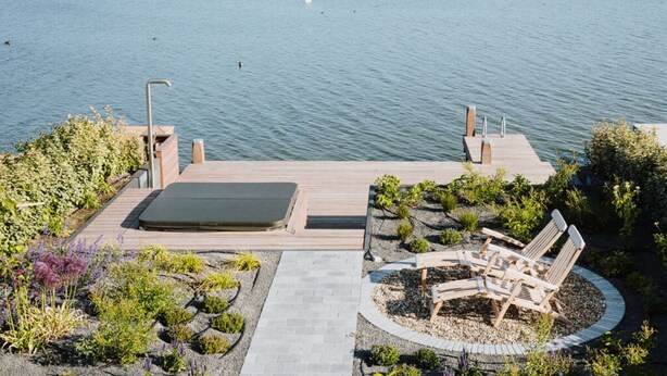 A wooden deck with a hot tub and lounge chairs by a lake. - Oceanhouse Comfortable Holiday Residence (Wieringerwerf)