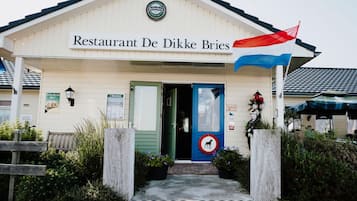 A building labeled "Restaurant De Dikke Bries" with a blue door, a Heineken sign, and a red and white flag.