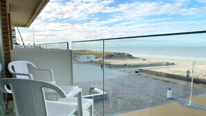 A balcony with white plastic chairs, a glass barrier, a view of the beach, and a sandy walkway. - Apartment in Nieuwpoort With Garden (Nieuwpoort)