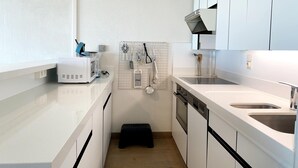 A modern kitchen with white cabinets, a built-in oven, a microwave, and a sink. - Apartment in Nieuwpoort With Garden (Nieuwpoort)