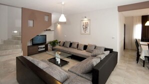 Ein modernes Wohnzimmer mit einer Eckcouch, einem Glastisch, einem Flachbildfernseher und einer Treppe, die zu einer anderen Ebene führt.