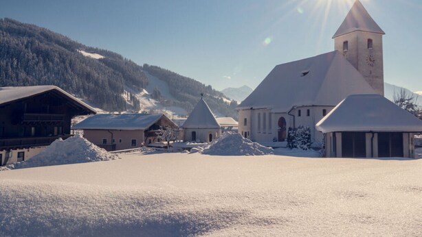 A snow-covered village with a prominent church featuring a tall tower and a clock. - Apartment Bar Comfortable Holiday Residence (Eben im Pongau)