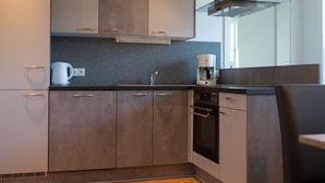 A modern kitchen with dark wooden cabinets, a built-in oven, and a coffee maker. - Apartment Bar Comfortable Holiday Residence (Eben im Pongau)