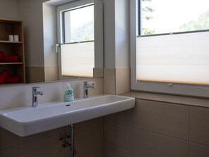 Une salle de bain avec un lavabo blanc, un miroir et une fenêtre avec des stores.