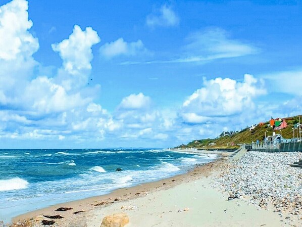 A beach with waves, a clear sky, and a rocky shoreline.