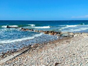 A pebbled beach with waves crashing onto rocks. - 6 Person Holiday Home in Graested (Graested)