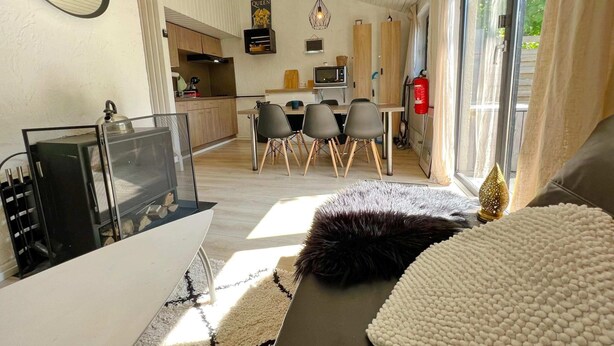 A modern living room with a sofa, a coffee table, and a television. There is a kitchen area with a dining table and chairs.