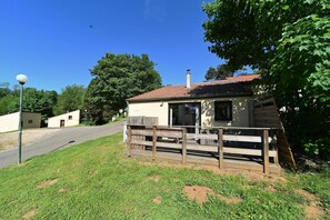 Une petite cabane à un seul étage, avec un toit recouvert de tuiles rouges, une terrasse en bois et un porche à l’avant.