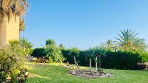 Un jardín bien cuidado con una mesa de picnic, un elemento decorativo de piedra circular y diversas plantas y árboles.