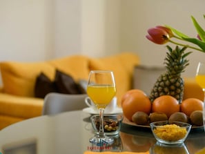 Une table avec un verre de jus d’orange, un bol de noix, un bol de céréales, un ananas, des oranges et une tulipe.