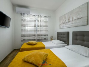 Quarto de hotel com duas camas, uma TV de tela plana, um quadro e uma janela com cortinas listradas.