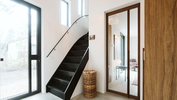 A modern interior with a black spiral staircase, large sliding glass doors, and a wicker basket. - Holiday Home for Family (Ouddorp)