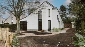 A modern white building with a sloped roof, a large glass door, and a small patio area with two chairs. - Holiday Home for Family (Ouddorp)