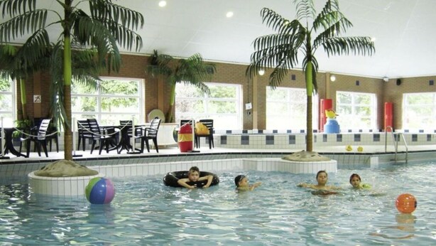 An indoor swimming pool with clear water, surrounded by lounge chairs and tables. - Holiday Home Deichblick 58 (Andijk)