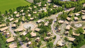 Vista aérea de un resort con varias cabañas de estilo bungalow dispuestas alrededor de una zona circular central, probablemente una piscina o espacio de encuentro.