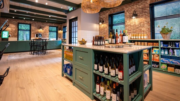 Zona de bar con suelo de madera, taburetes verdes y una variedad de botellas en estanterías.