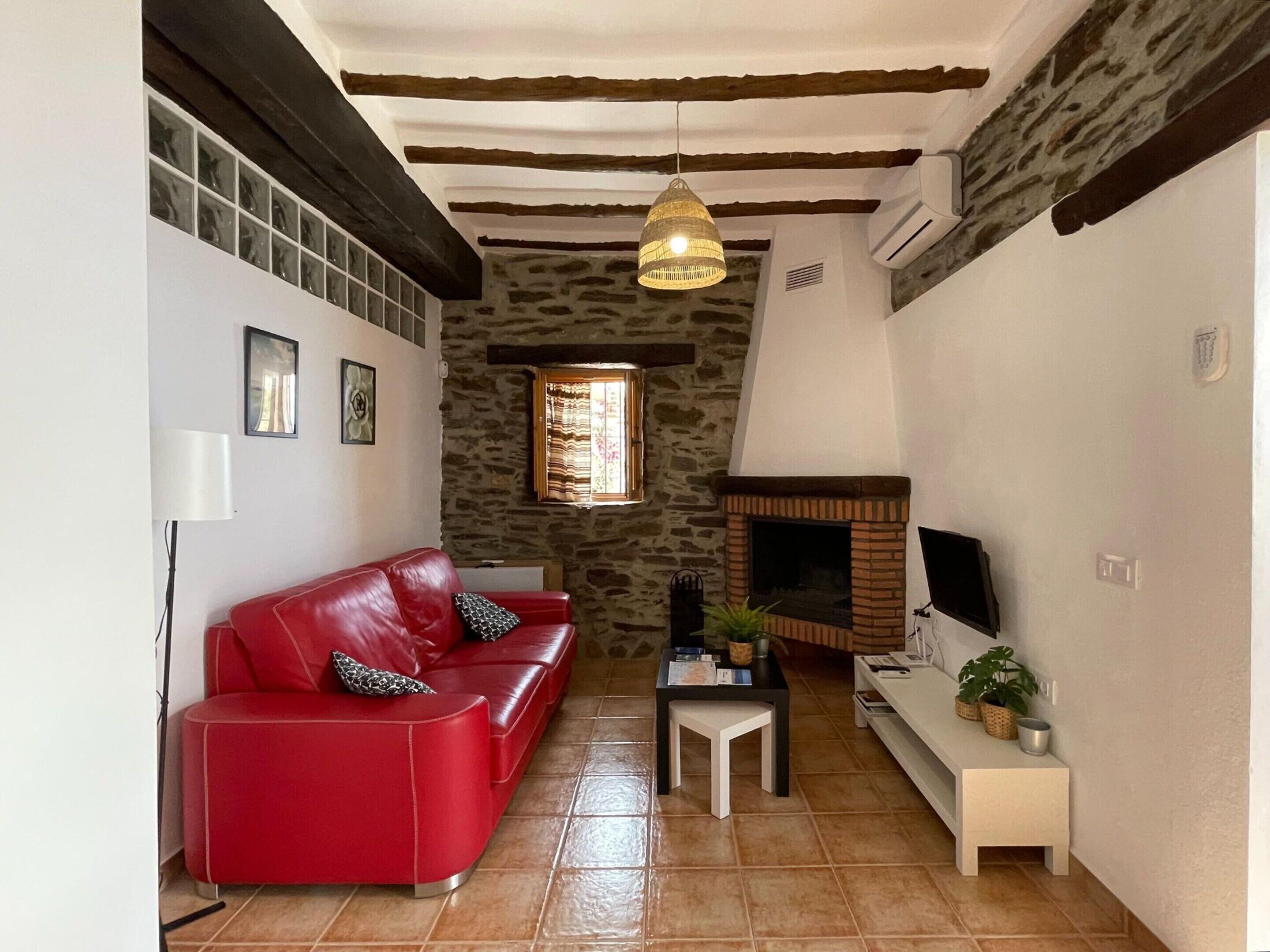 Un salon chaleureux avec un canapé en cuir rouge, un mur en pierre, une cheminée et un luminaire suspendu.