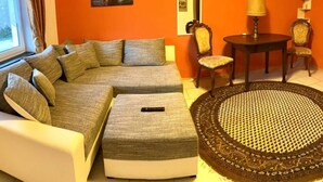 Ein Wohnzimmer mit einer Eckcouch, zwei Sesseln, einem runden Couchtisch und einem gemusterten Teppich.