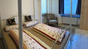 Ein Zimmer mit zwei Betten, einem Sessel und einem fenster mit Vorhängen.