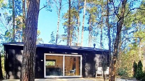 Una cabaña con un amplio ventanal corredera, un balcón y rodeada de altos árboles.