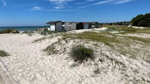 A row of beach huts with a sandy beach and dunes in the foreground, and a clear blue sky above.