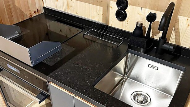 A kitchen with a black countertop, stainless steel sink, and a built-in oven.