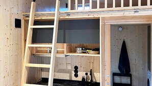 A wooden interior with a lofted sleeping area, a kitchen with a stove, and a door leading to another room.