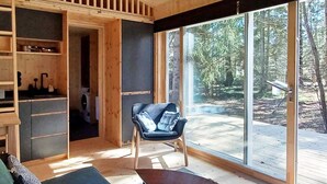 Un interior moderno con un sofá, una silla y una mesa en una habitación con ventanas grandes y vistas a árboles.
