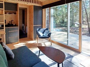 Un interior moderno con un sofá, una silla y una mesa en una habitación con ventanas grandes y vistas a árboles.