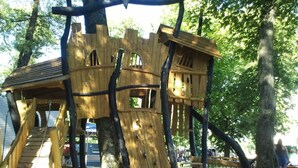 Een houten boomhut met een trap, gebouwd in een boom, omgeven door zand.
