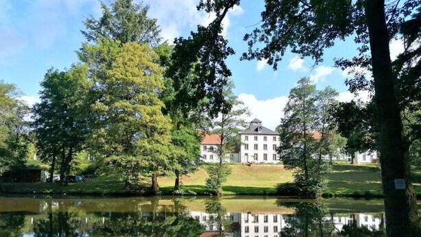 Een rustig uitzicht op een meer met een groot wit gebouw op de achtergrond, omringd door weelderige begroeiing en bomen.