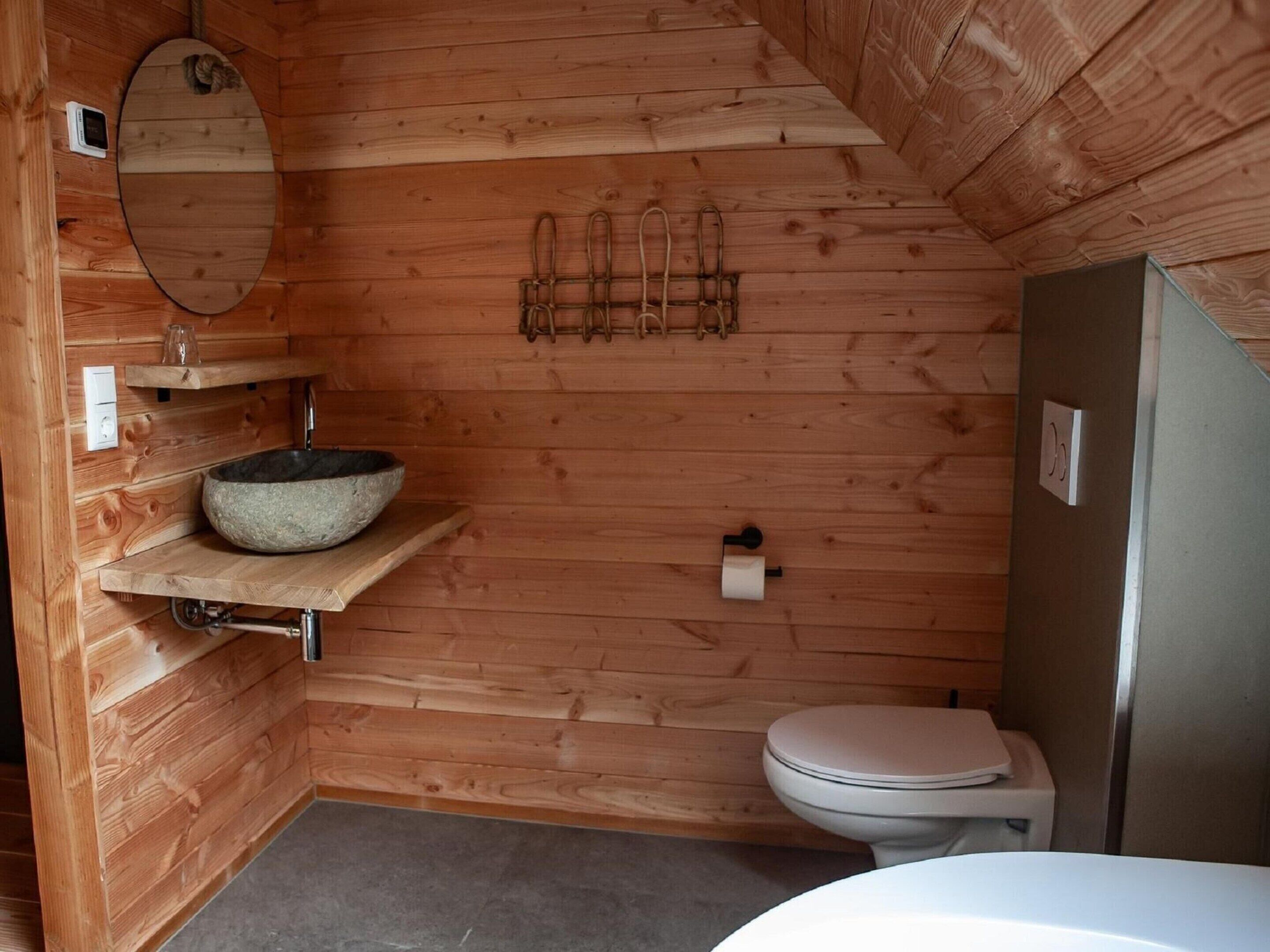 Baño de cabaña de madera con un lavabo de piedra, un inodoro y un espejo.