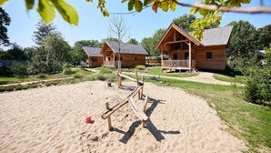 A wooden cabin with a deck, surrounded by a sandy area and greenery. - Holiday Home in Brabant With Private Spa (Uden)
