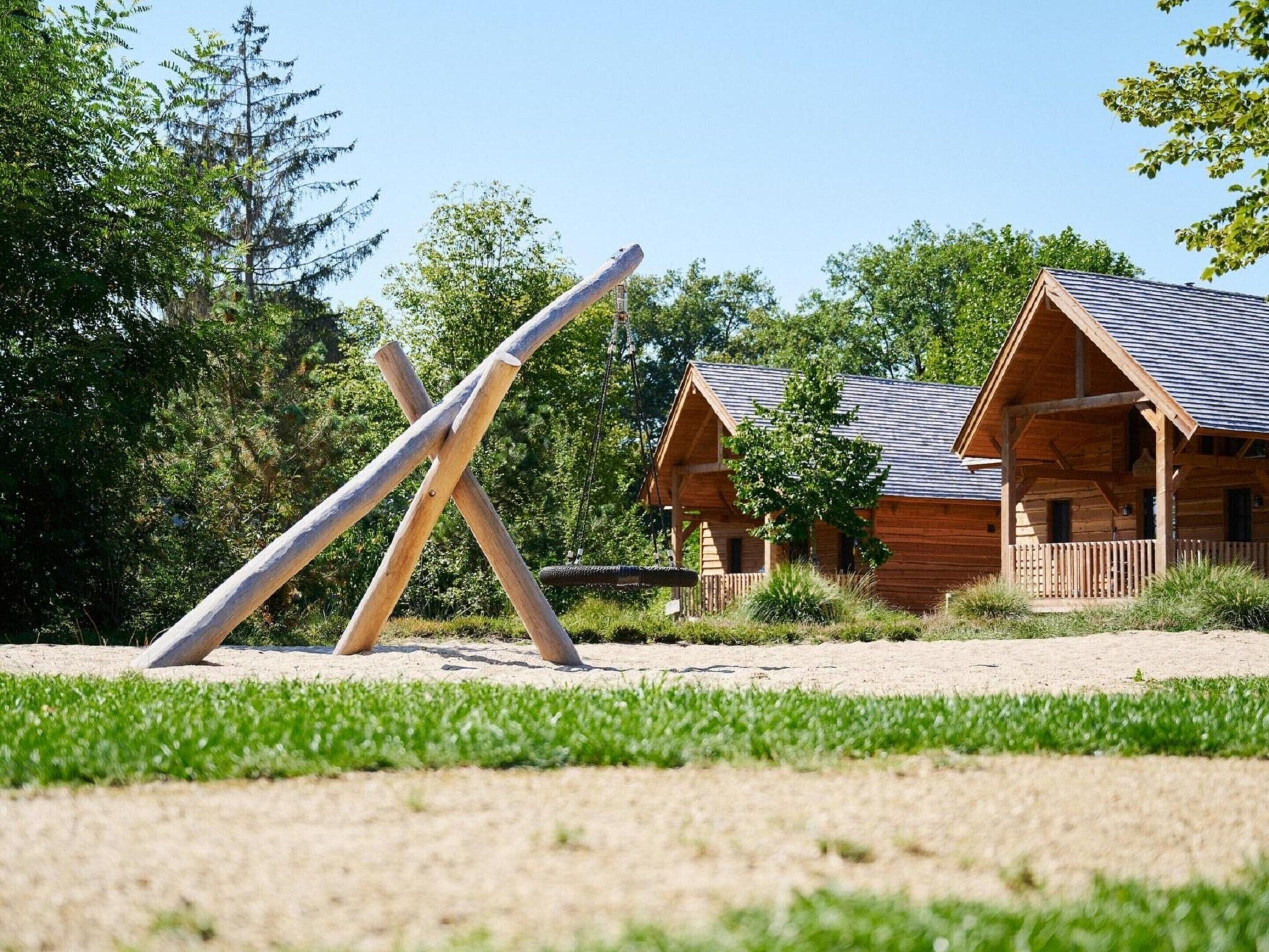 A rustic wooden cabin with a sloped roof and a porch, surrounded by a grassy area and trees.