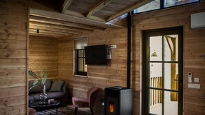 A cozy wooden cabin interior with a sofa, armchair, and a fireplace. - Holiday Home in Brabant With Private Spa (Uden)