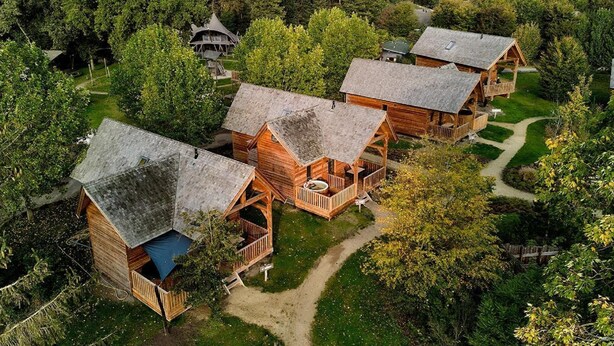 A cluster of wooden cabins with thatched roofs, surrounded by dense forest, connected by pathways. - Holiday Home in Brabant With Private Spa (Uden)