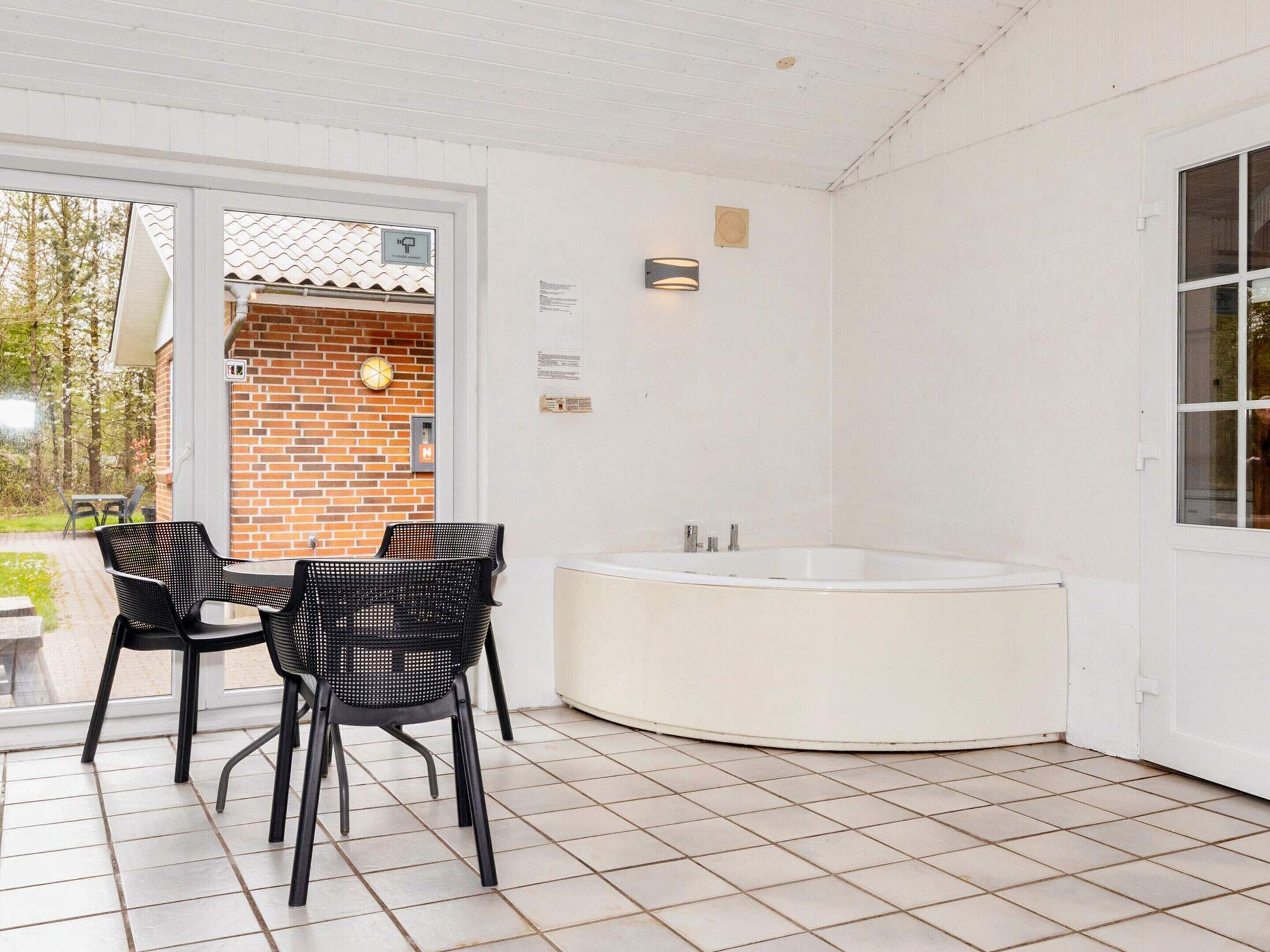 Een terras buiten met een tafel, stoelen, een bakstenen muur en een witte deur.