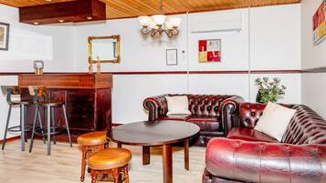 Quarto com teto de madeira, mesa redonda, sofá de couro, dois banquinhos de madeira, área de bar com espelho e obras de arte fixadas na parede.