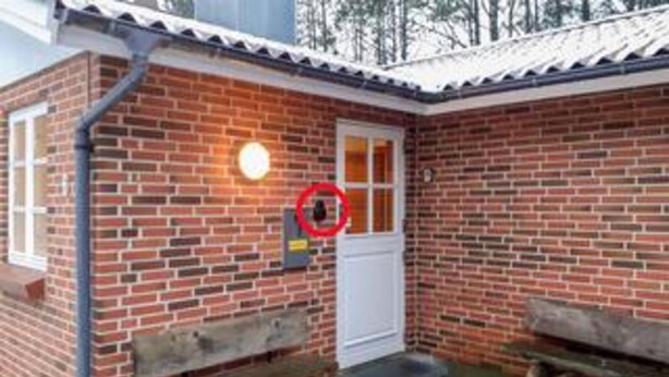 Ein kleines Backsteinhaus mit einer weißen Tür, einer Bank davor und einem roten Kreis, der einen bestimmten Bereich kennzeichnet.
