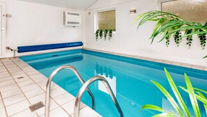 Ein überdachter Pool mit blauen Fliesen, einer Metallleiter und einer weißen Wand mit Fenster und Wandklimaanlage.