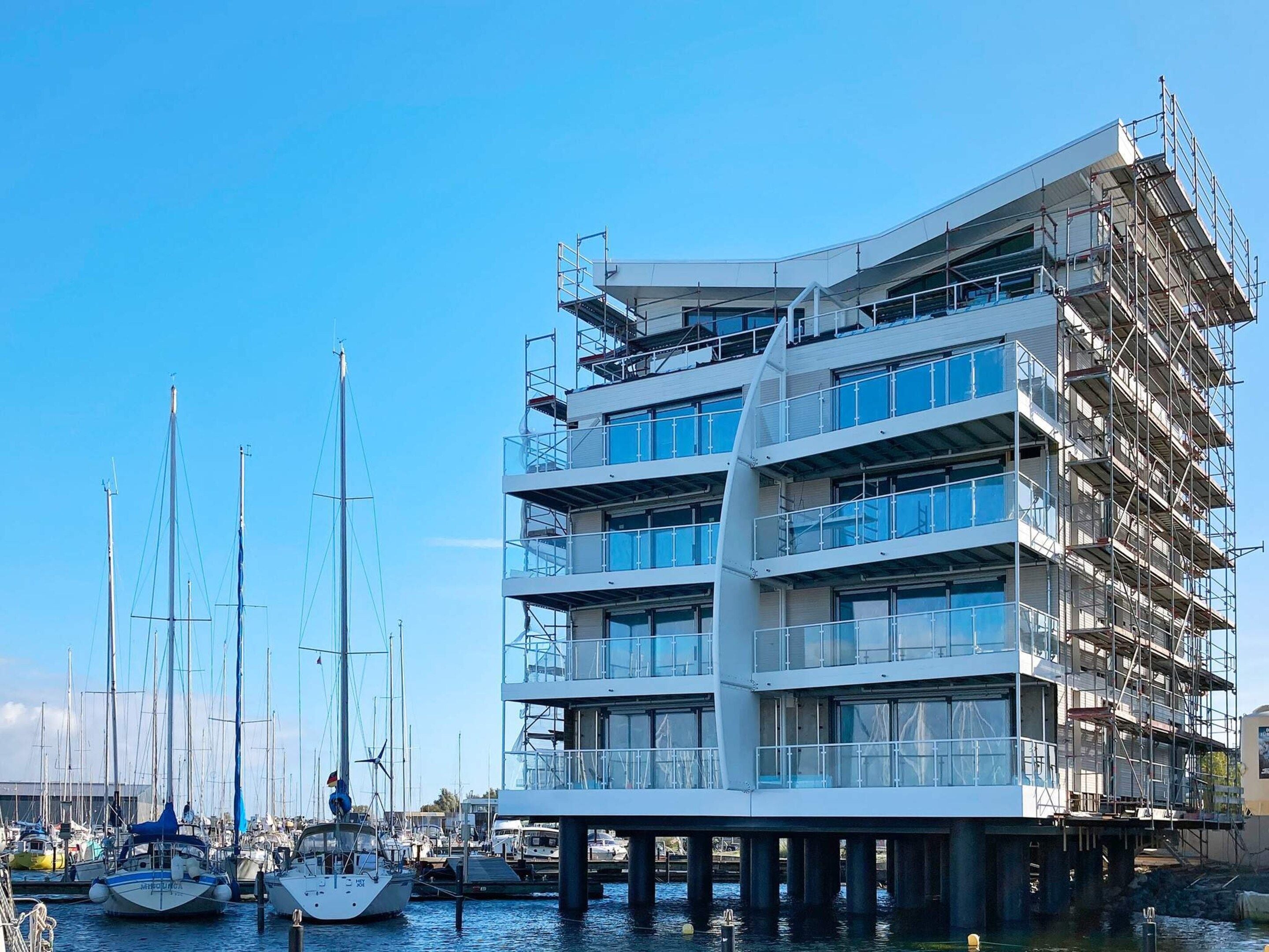 A multi-story building with a modern architectural design, located adjacent to a marina with several boats.