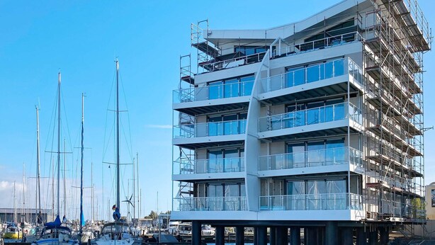 A multi-story building with a modern architectural design, located adjacent to a marina with several boats. - Holiday Home in Wendtorf (Wendtorf)