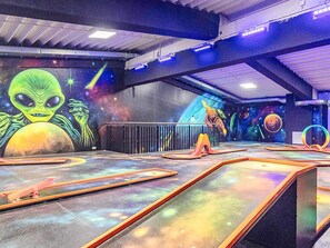Un espace intérieur décoré d’une fresque murale sur le thème de l’espace, représentant notamment un extraterrestre et des planètes, ainsi qu’un espace de jeux avec des structures colorées.