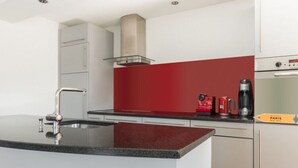 Une cuisine moderne dotée d’un plan de travail en granit, d’appareils électroménagers en acier inoxydable et d’un crédence rouge.